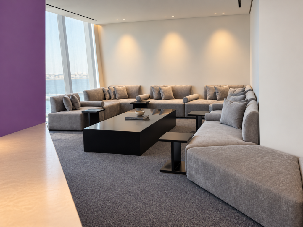 Modern office waiting majlis featuring a custom curved grey sofa and low-profile black lacquer coffee tables by windows.